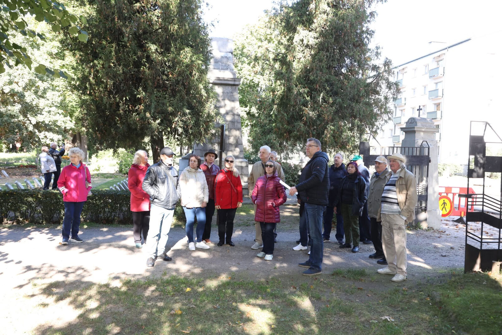 Dalībnieku grupa pie vēsturiska piemiņas vietas vārtiem pilsētas parkā