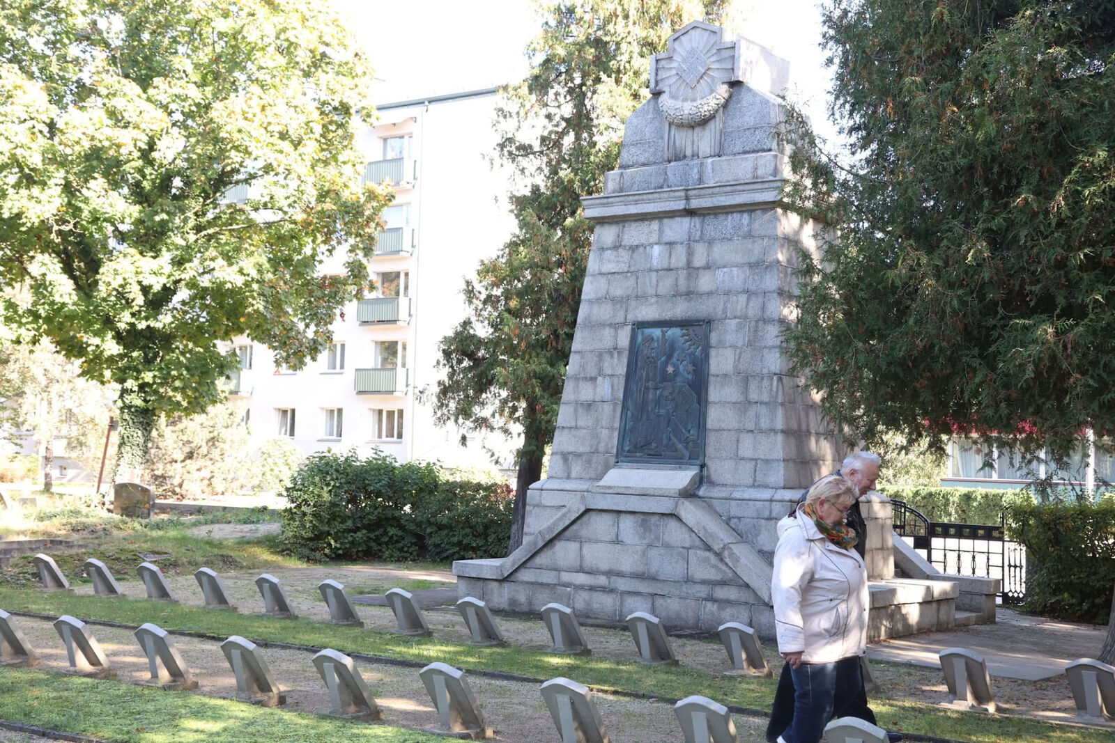Akmens piemineklis ar bronzas plāksni, priekšplānā rindās izvietotas piemiņas zīmes